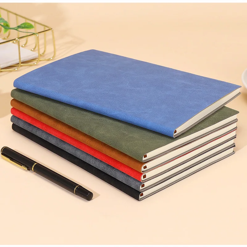 Stack of softcover notebooks in several colors with a pen